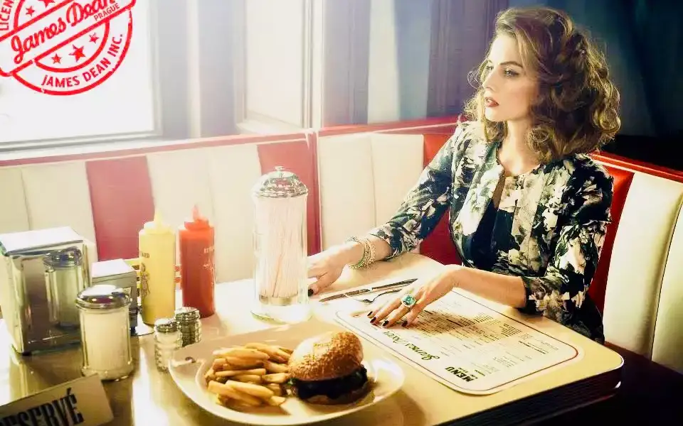 Modelka u okna v boxu dineru, na stole burger s hranolky