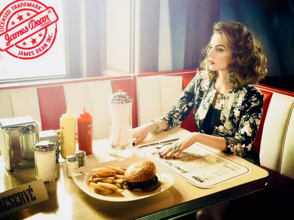 Modelka u okna v boxu dineru, na stole burger s hranolky