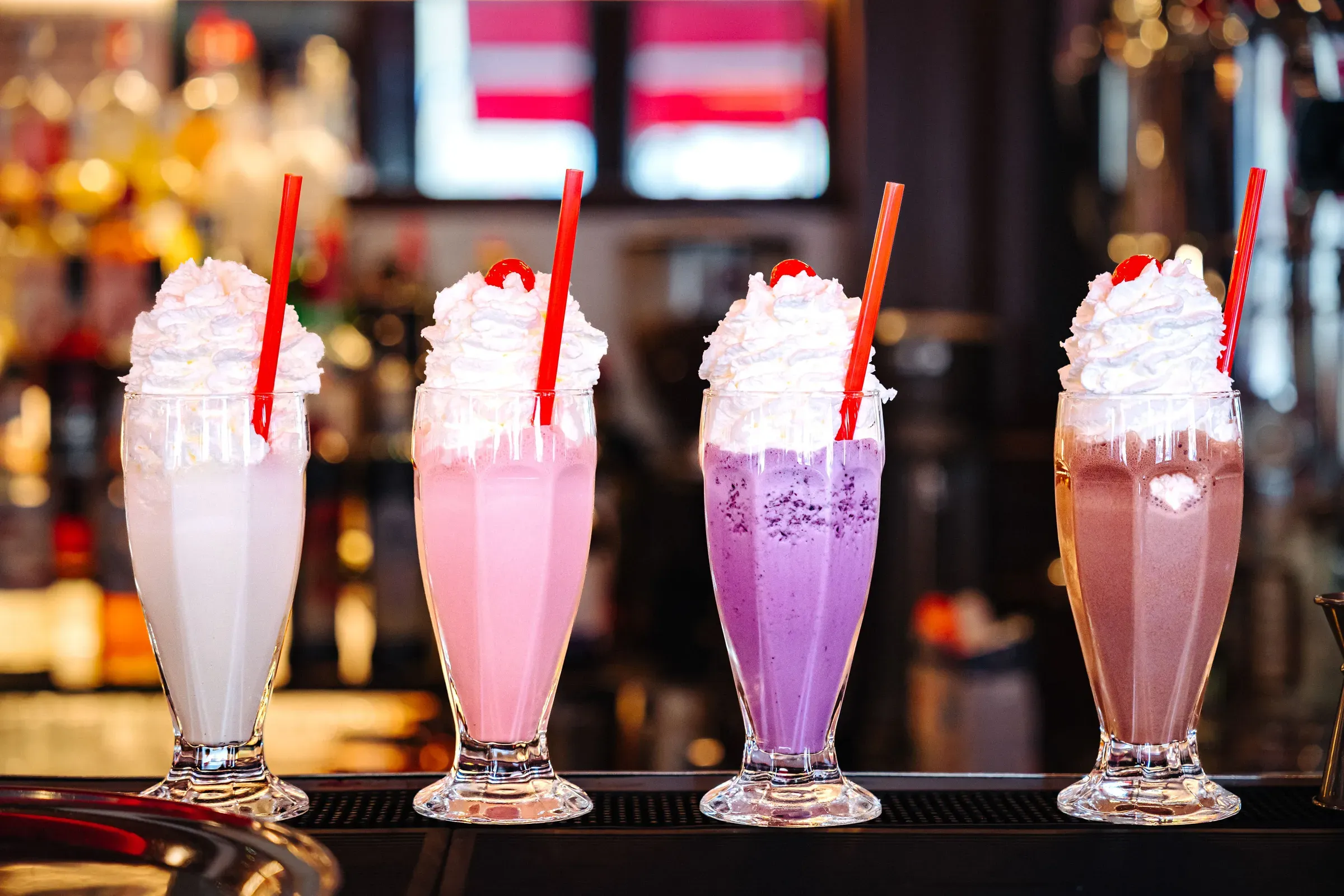Čtyři milkshaky se šlehačkou a červenými brčky na baru