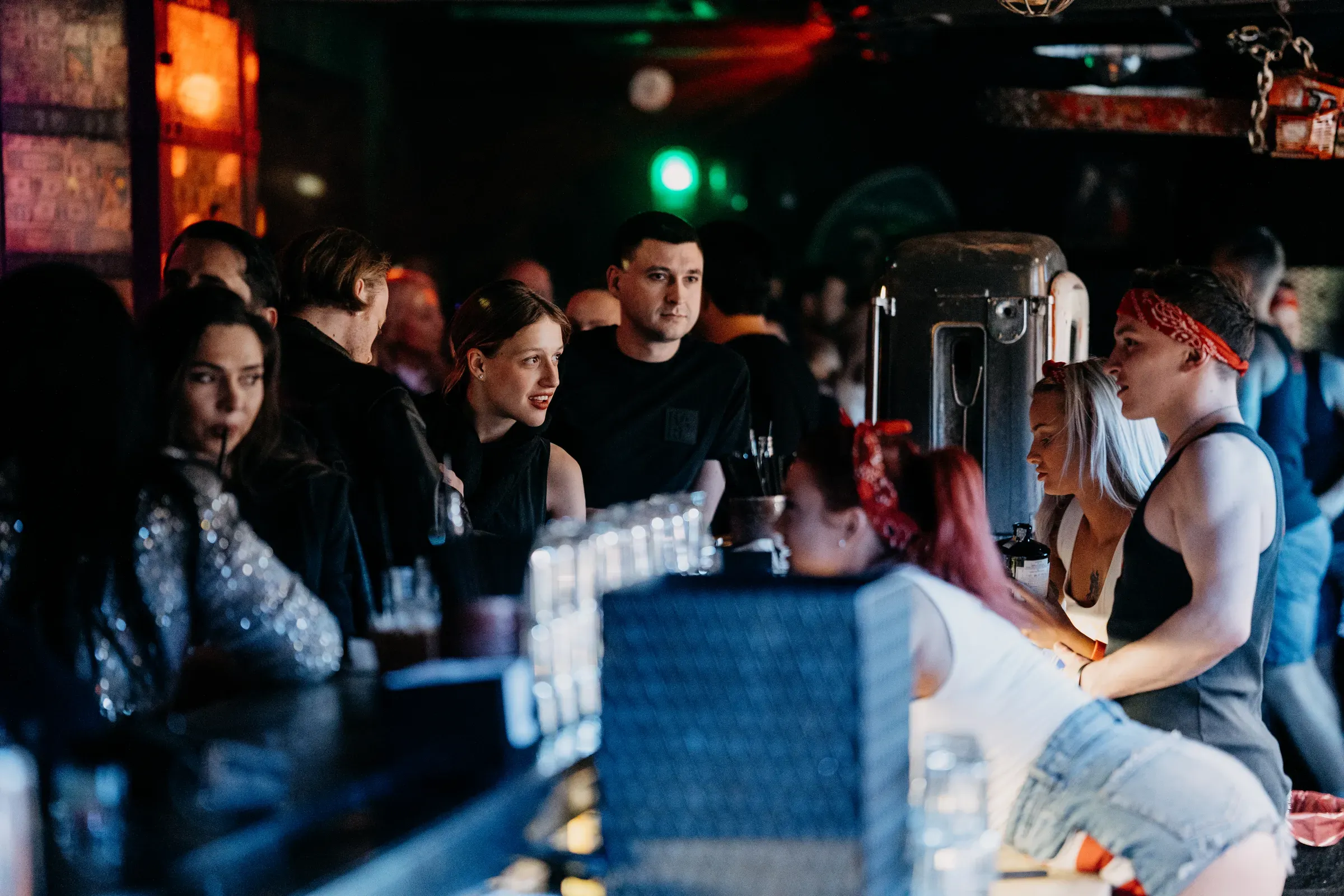 Hosté u baru Music Clubu a barmani s červenými šátky ve vlasech