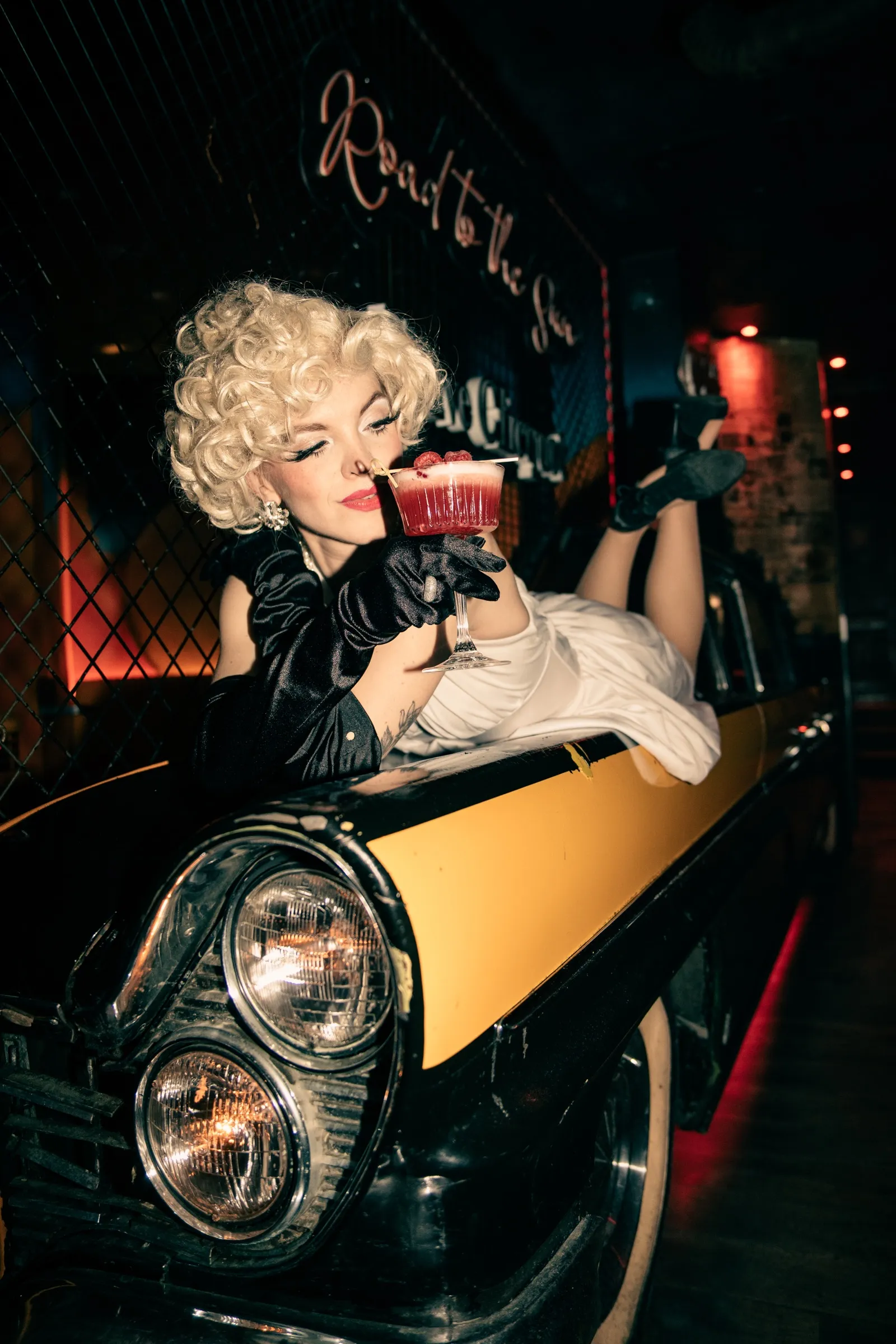 Modelka ve stylu Marilyn Monroe s koktejlem na kapotě amerického auta v Music Clubu