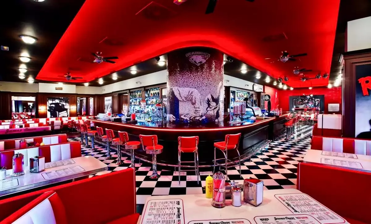 Interiér restaurace James Dean: červené barové židle, šachovnicová podlaha a mozaikový sloup
